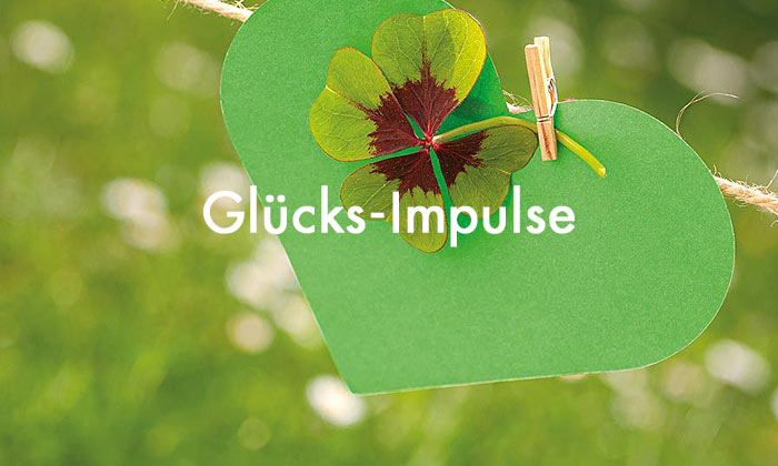 weiße Schrift Glücksimpulse - im Hintergrund ein vierblättriges Kleeblatt mit Holzklammer an einer Schnur