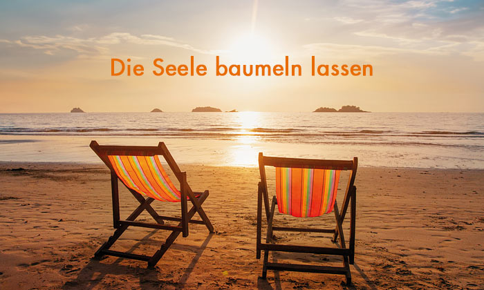 orangefarbene Schrift Die Seele baumeln lassen - im Hintergrund zwei Leinenliegestühle am Strand mit untergehender Sonne