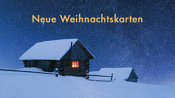 hellgelbe Schrift Neue Weihnachtskarten - im Hintergrund eine verschneite Berghütte in der Nacht mit einem beleuchtetem Fenster