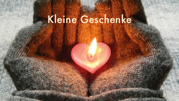 hellgelbe  Schrift Kleine Geschenke - im Hintergrund zwei Hände in Wollhandschuhen, die ein herzförmiges Teelicht halten