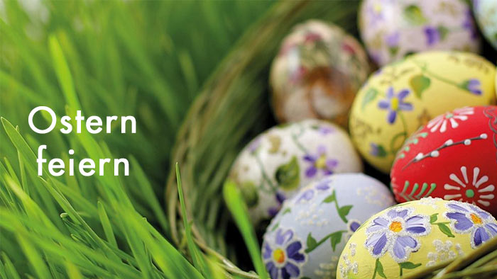 zur Themenseite Ostern feiern weiße Schrift Ostern feiern - im Hintergrund buntbemalte Ostereier in einem Korb im Gras