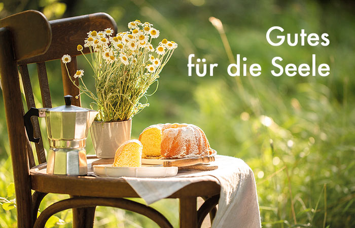 weiße Schrift Gutes für die Seele - im Hintergrund ein Stuhl mit einer Kaffeekanne, einem Kuchen und einem Margeritenstrauß
